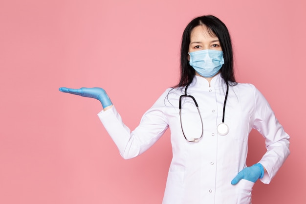 młoda kobieta w białym garniturze medycznych niebieskie rękawiczki niebieska maska ochronna ze stetoskopem na różowo