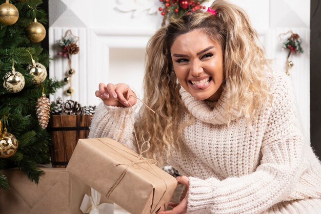 Młoda kobieta w białym swetrze przedstawiająca dwa pudełka prezentów świątecznych.
