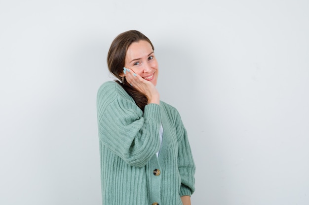 Młoda kobieta w bluzce, sweterek opierając policzek na dłoni i patrząc z wdziękiem, widok z przodu.