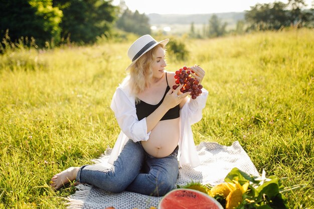 Młoda kobieta w ciąży relaks w parku na świeżym powietrzu i jedzenie arbuza, zdrowa ciąża