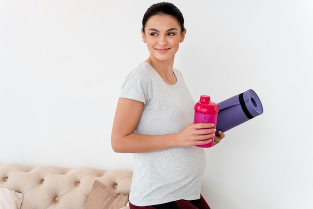 Młoda kobieta w ciąży trzyma matę fitness