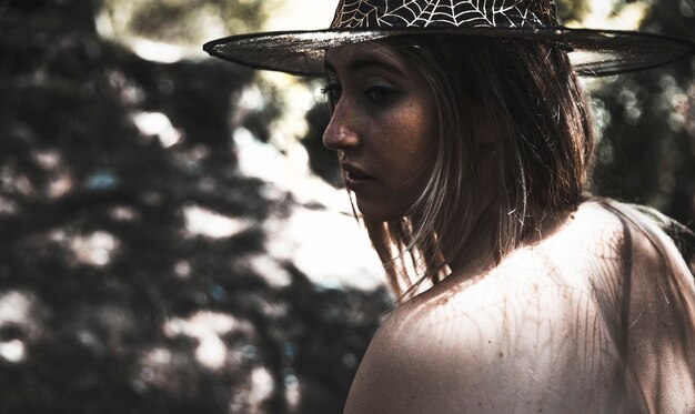 Młoda kobieta w czarownica kapeluszu w mrocznym lesie