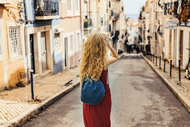 Młoda kobieta w czerwonej sukience idąca drogą otoczoną budynkami w słońcu under