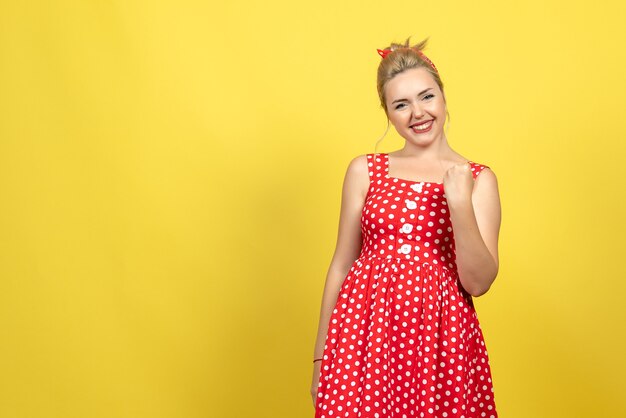młoda kobieta w czerwonej sukience w kropki pozowanie i uśmiechając się na żółto