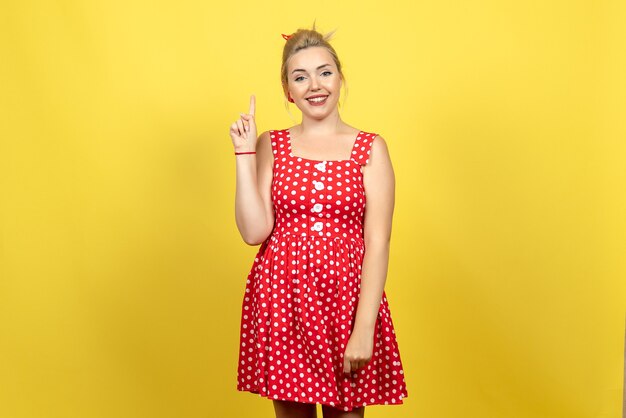 młoda kobieta w czerwonej sukience w kropki uśmiechając się na jasnożółtym