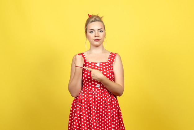 młoda kobieta w czerwonej sukience w kropki wskazując jej nadgarstek na żółto