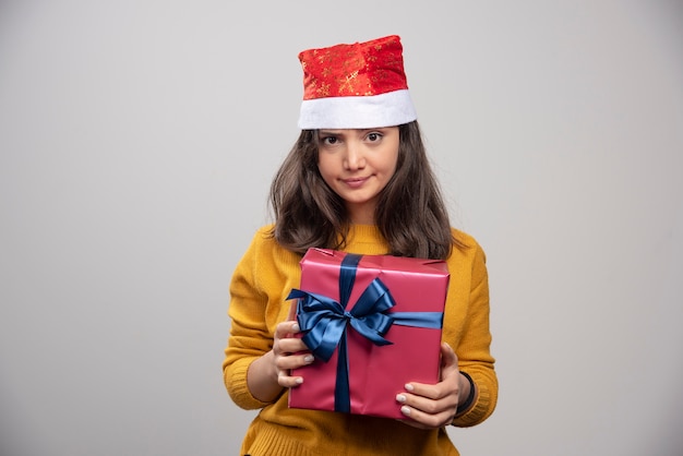Młoda kobieta w czerwonym kapeluszu Świętego Mikołaja z prezentem bożonarodzeniowym.