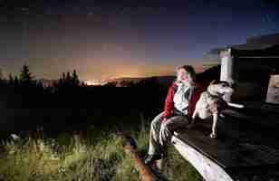 Bezpłatne zdjęcie młoda kobieta w górach ogląda piękną gwiaździstą noc z werandy drewnianej chaty