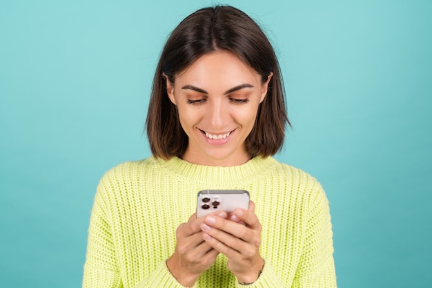 Młoda kobieta w jasnozielonym swetrze z telefonem komórkowym z uśmiechem pisania wiadomości