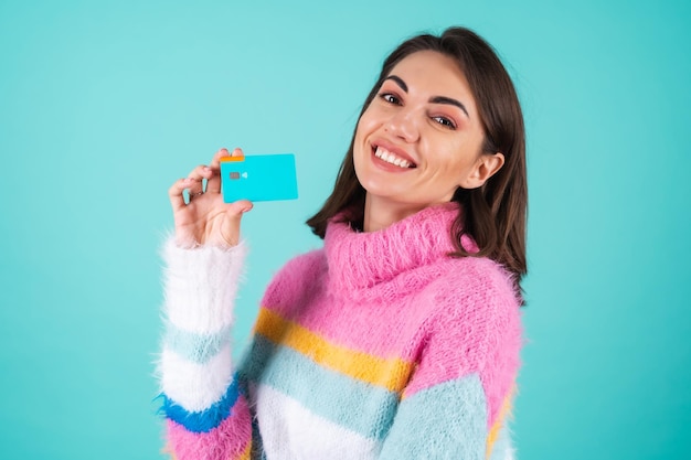 Młoda kobieta w jasnym wielokolorowym swetrze na niebiesko pokazuje kartę kredytową z pustym miejscem