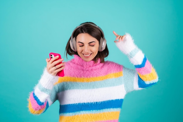 Młoda kobieta w jasnym wielokolorowym swetrze na niebiesko w dużych słuchawkach z funkcją redukcji hałasu