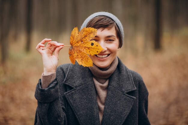 Młoda kobieta w jesiennym parku trzymając liść przy twarzy