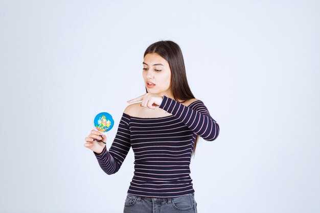 Młoda kobieta w koszuli w paski, trzymając mini kulę ziemską i odgadując miejsce nad nią