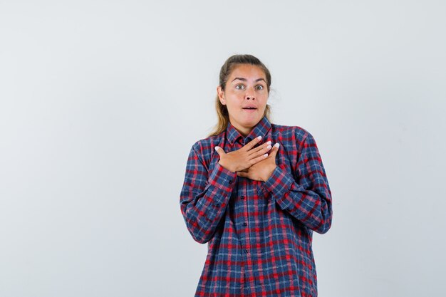 Młoda kobieta w kraciastej koszuli, opierając ręce na klatce piersiowej i patrząc zdziwiony
