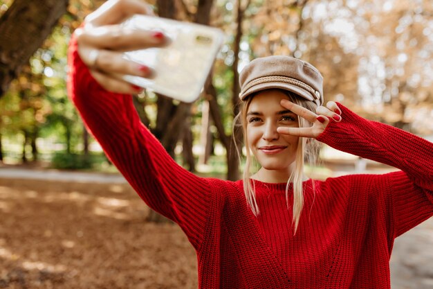 Młoda kobieta w ładny czerwony sweter sprawia, że selfie na ścieżce w parku.