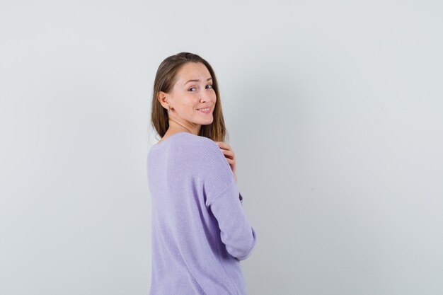 Młoda kobieta w liliowej bluzce, patrząc wstecz i wyglądająca imponująco
