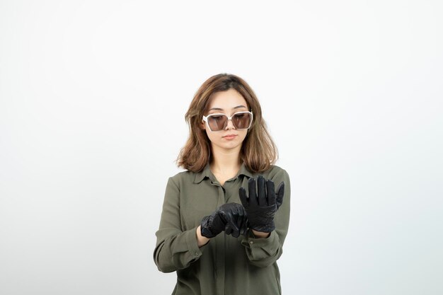 Młoda kobieta w okularach próbuje na czarnych rękawiczkach na białym. Zdjęcie wysokiej jakości