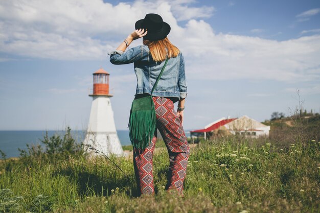 Młoda kobieta w przyrodzie, latarnia morska, czeski strój, dżinsowa kurtka, czarny kapelusz, lato, stylowe dodatki