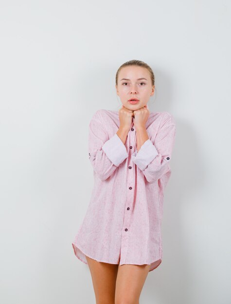 Młoda kobieta w różowej koszuli podpierając brodę na pięści i patrząc zaciekawiony