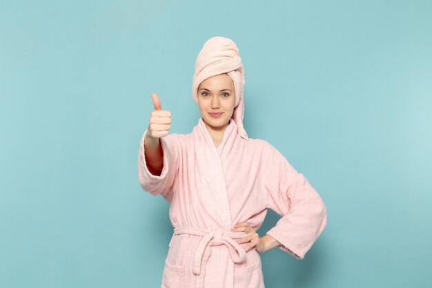 młoda kobieta w różowym szlafroku po prysznicu pozowanie z twarzą uśmiech na niebiesko