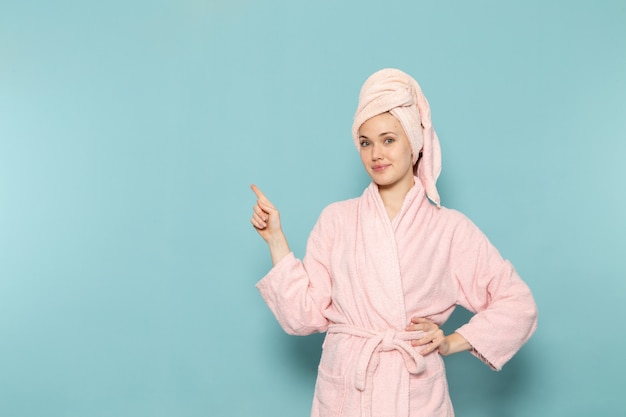 młoda kobieta w różowym szlafroku po prysznicu tylko pozuje z uśmiechem na niebiesko