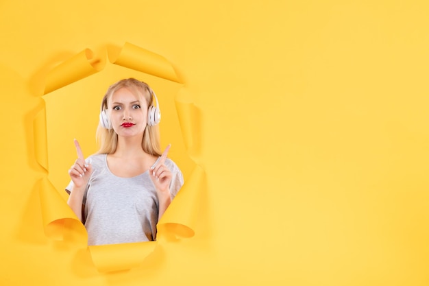 Młoda kobieta w słuchawkach na rozdartym żółtym papierze w tle muzyka ultradźwiękowe dźwięki audio