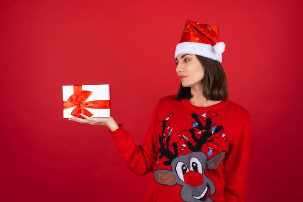 Młoda kobieta w świątecznym swetrze i czapce Mikołaja z pudełkiem na prezent