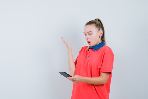 Młoda kobieta w t-shirt patrząc na telefon komórkowy i patrząc niespokojny