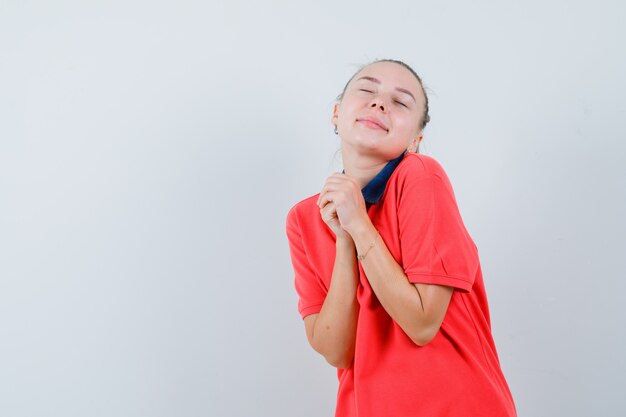 Młoda kobieta w t-shirt, trzymając ręce splecione i patrząc spokojnie