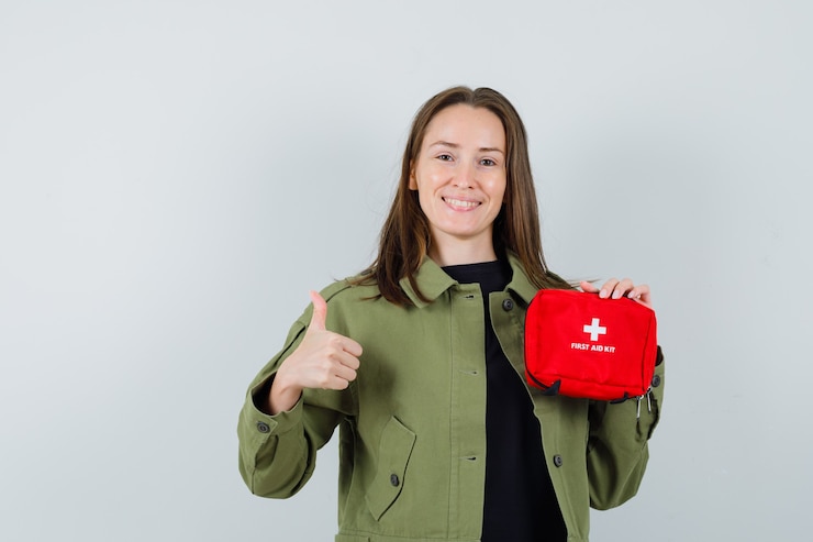 Bezpłatny plik Zdjęcie młoda kobieta w zielonej kurtce trzymając apteczkę, pokazując kciuk w górę i patrząc zadowolony, widok z przodu.