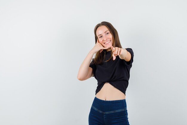 Młoda kobieta, wskazując na aparat, pokazując gest telefonu w czarnej bluzce