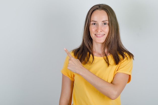 Młoda kobieta wskazując palcem do tyłu w żółtej koszulce i patrząc wesoło