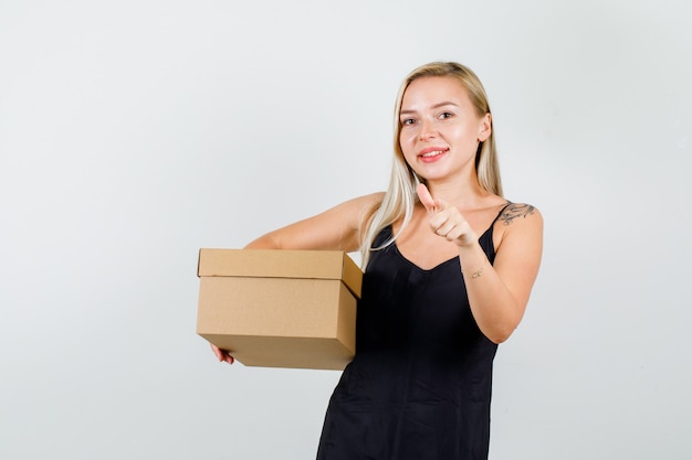 Młoda kobieta wskazując palcem na aparat z pudełkiem w czarnym podkoszulku i patrząc szczęśliwy
