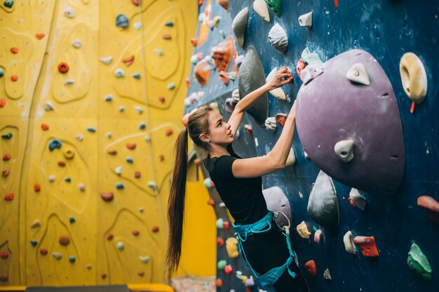 Młoda kobieta wspinająca się po wysokiej, sztucznej sztucznej skalnej ścianie wspinaczkowej