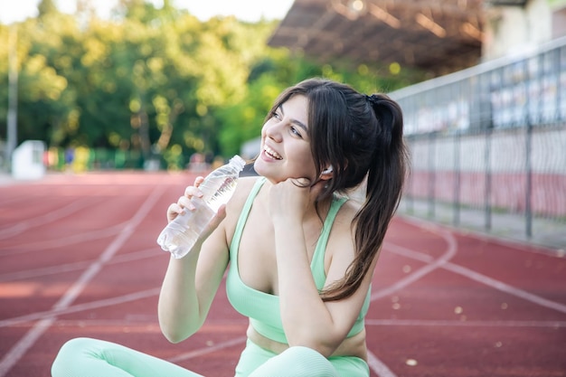 Młoda kobieta z butelką wody podczas treningu na stadionie
