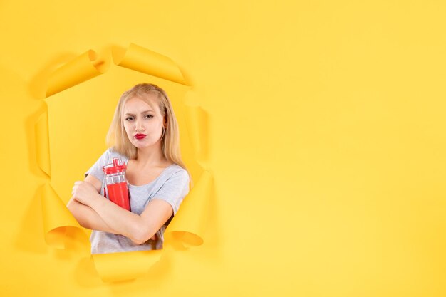Młoda kobieta z czerwoną butelką na żółtym tle sportowiec sport fit siłowni maseczki na twarz