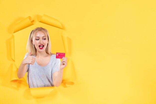Młoda kobieta z czerwoną kartą kredytową na rozdartej żółtej powierzchni papieru
