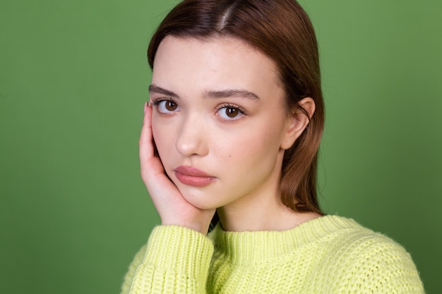 Młoda kobieta z czystą idealną naturalną skórą i makijażem brązowe duże usta na zielonej ścianie niezadowolony smutny rozczarowany