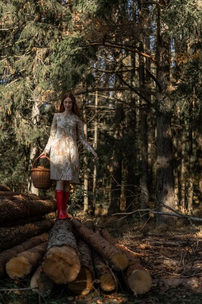 Młoda kobieta z długimi rudymi włosami w lnianej sukience zbierając grzyby w lesie