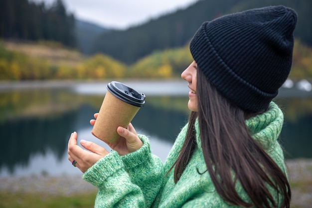 Bezpłatne zdjęcie młoda kobieta z filiżanką kawy na rozmytym tle gór