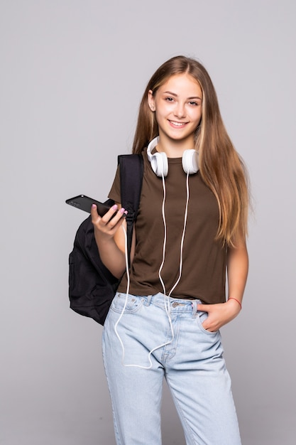 Młoda kobieta z inteligentny telefon słuchać muzyki z plecakiem na białym tle na białej ścianie