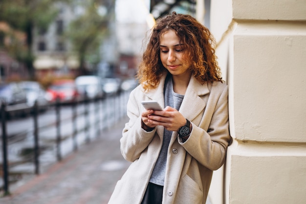 Młoda kobieta z kędzierzawym włosy używać telefon przy ulicą