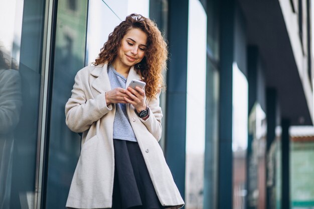 Młoda kobieta z kędzierzawym włosy używać telefon przy ulicą