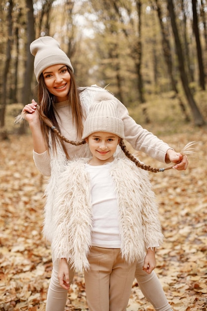 Młoda kobieta z małą dziewczynką spaceru w lesie jesienią. Brunetki kobieta bawi się z córką. Dziewczyna ubrana w beżowy sweter i matka ubrana w białe ubranie.