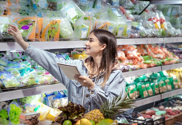 Młoda kobieta z notesem kupuje artykuły spożywcze w supermarkecie