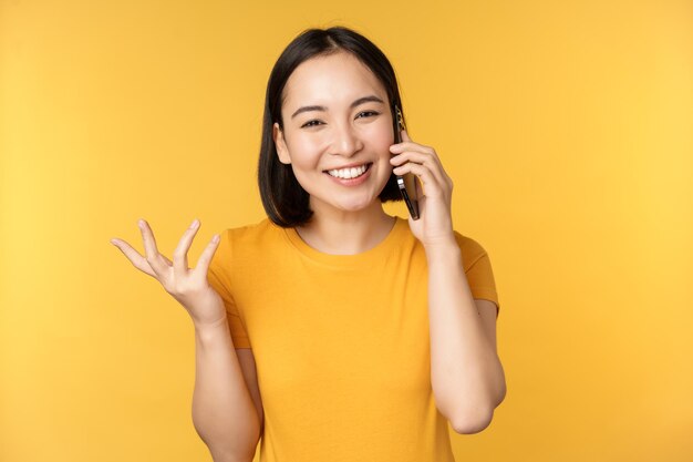 Młoda koreańska dziewczyna rozmawia przez telefon komórkowy Azjatycka kobieta dzwoni na smartfona stojącego na żółtym tle