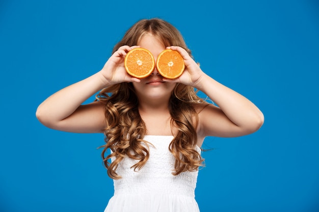 Młoda ładna dziewczyna chuje oczy dowcip pomarańcze nad błękit ścianą