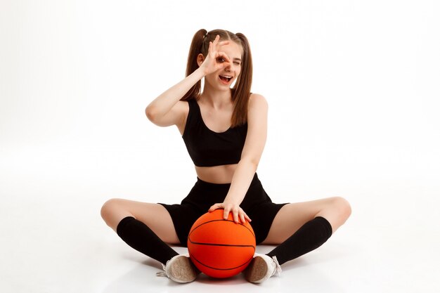 Młoda ładna dziewczyna pozuje z koszykówką nad biel ścianą