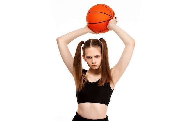Młoda ładna dziewczyna pozuje z koszykówką, odizolowywającą na biel ścianie