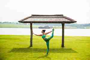Bezpłatne zdjęcie młoda ładna kobieta robi joga w porannym parku w pobliżu jeziora